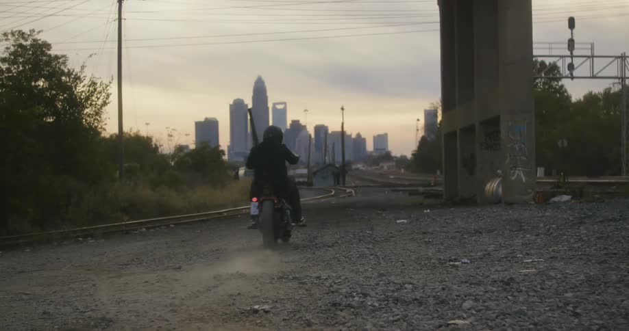Man driving a motorcicle under a bridge in front of the city skyline at sunset
