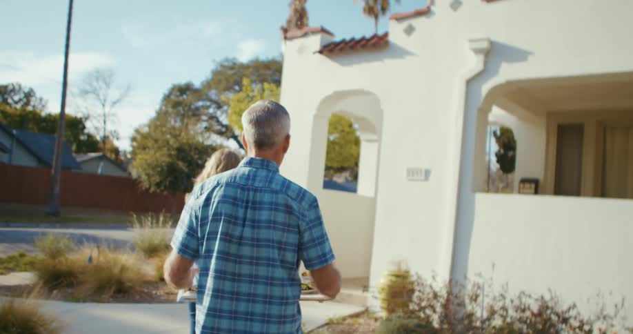 Couple approach red roof tiled house carrying tray of food