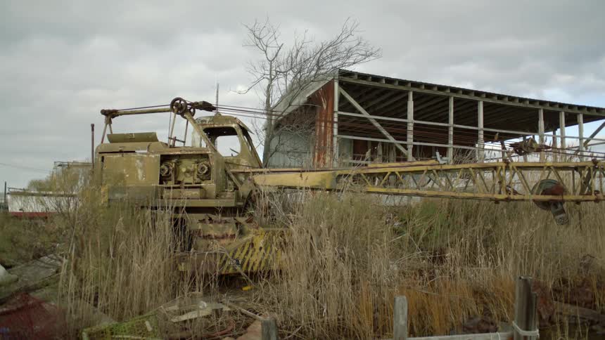 A derelict construction crane near a ruined building in a field on a cloudy day