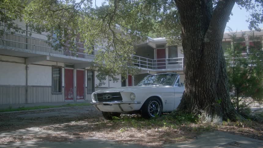White convertible car sits parked next to a tree near a motel
