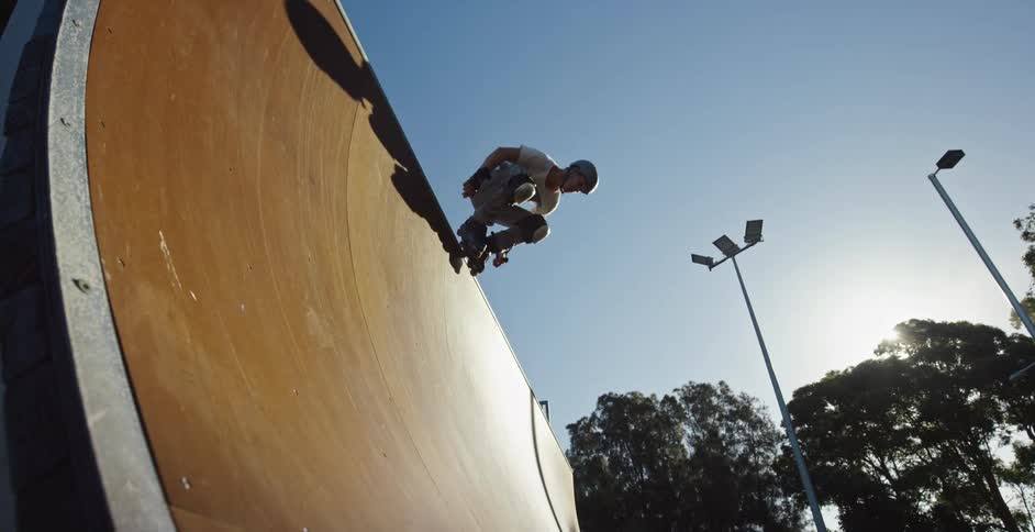 A man in a skate park skating with in line skates with trees the sky and clouds in the background