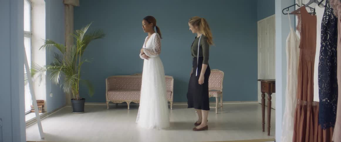 A woman is getting fitted for a wedding gown by an assistant in a shop