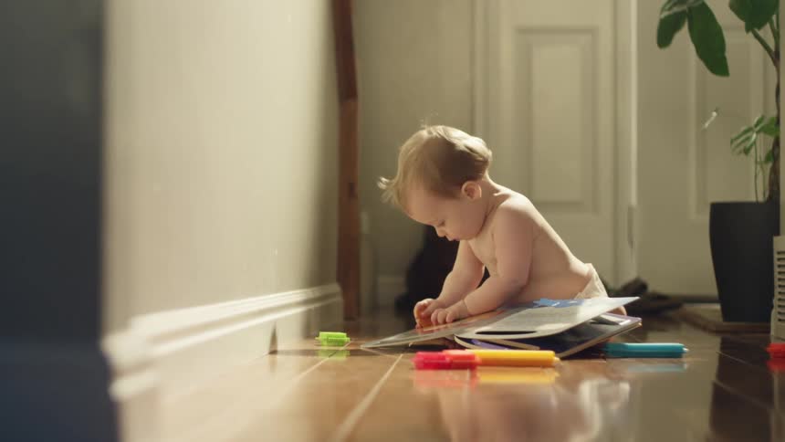 A baby sits on the floor at home and looks at a book