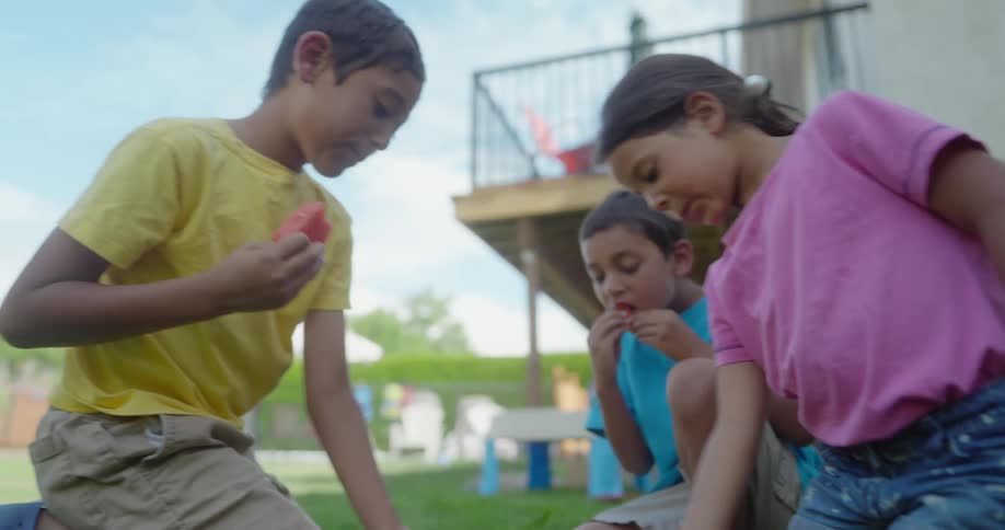 Group of kids eating watermelon slices over the grass in the backyard