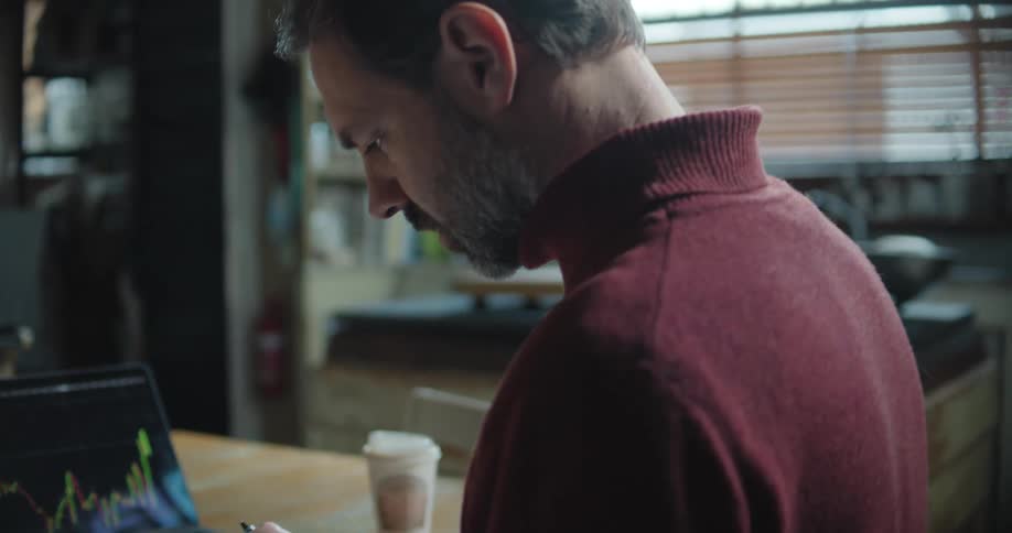 A man is sitting at a table with his cellphone and laptop