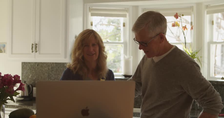 Blonde woman and man with glasses and grey sweatshirt cook talk to each other in the kitchen