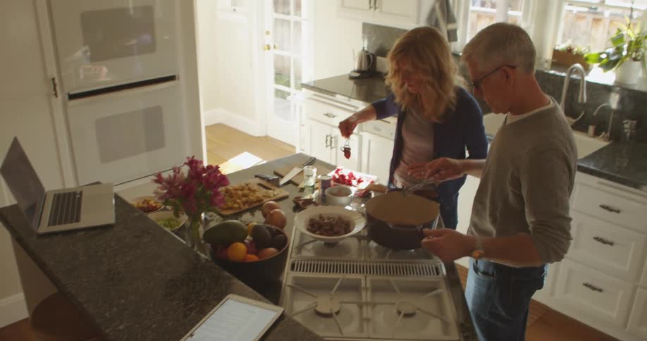 Husband and wife are cooking food together indoors