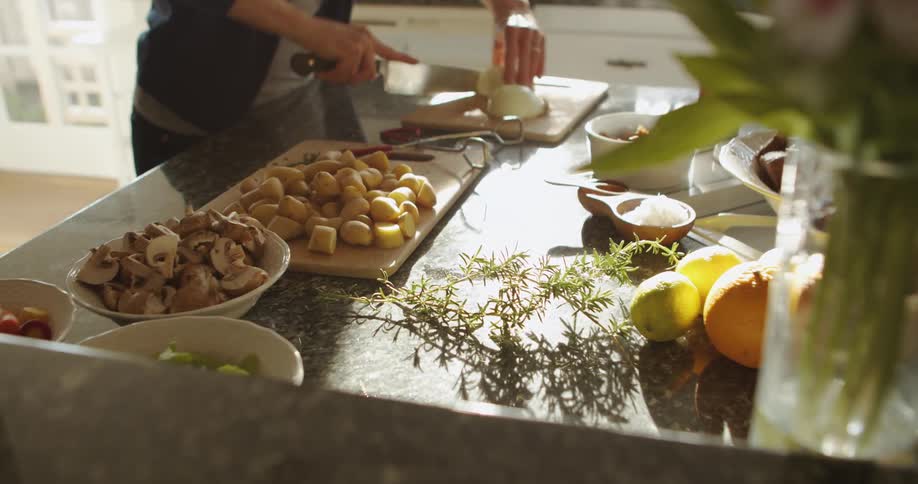 A woman cutting an onion on a cutting board next to other prepped vegetables