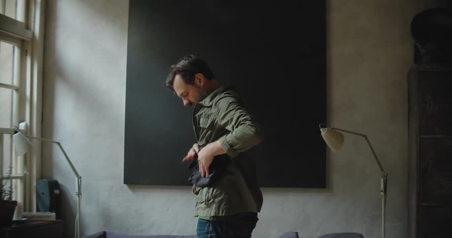 A man frantically searches for something in his cluttered house while patting down his pockets