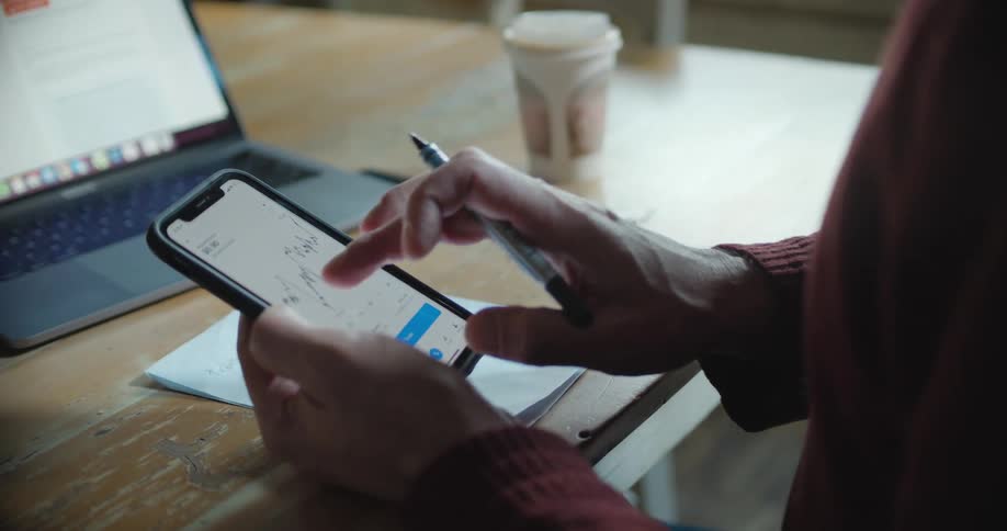 A person taps the screen of their smartphone to view a chart while sitting at a table