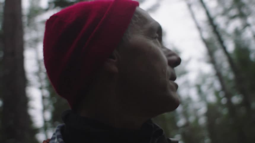 Man with a red beanie walks and looks around in the forest