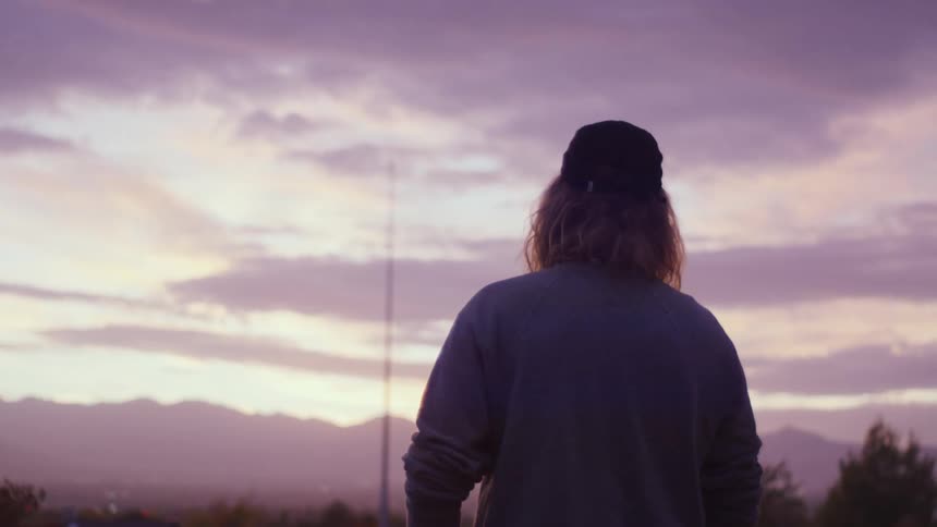 A man standing outside looks at the hills in the distance