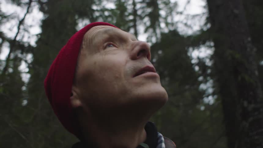Man with red beanie looks around in the woods