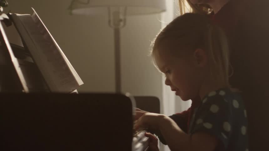 Woman teaches her young daughter to play the piano