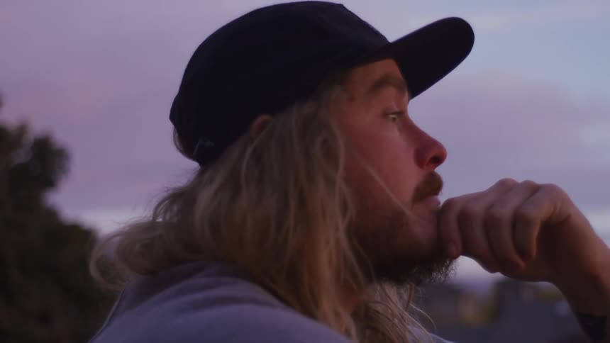 A man sits outdoors lost in thought at sunset