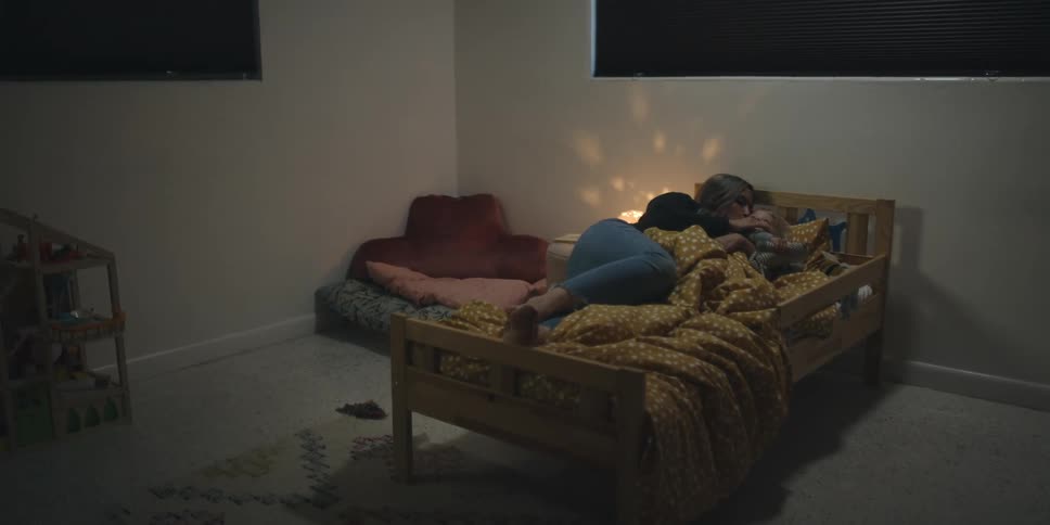 A woman and a child in a bedroom hugging and laying in bed with a wall and window in the background