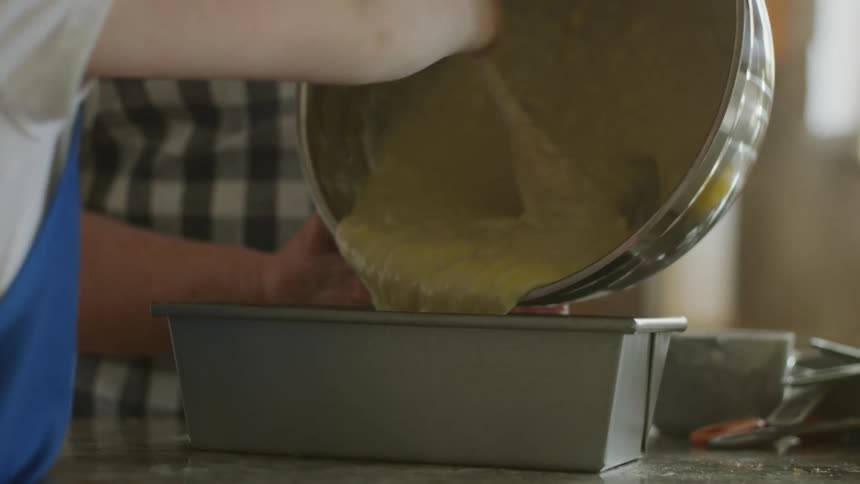 An adult holds a metal bowl while a child scrapes batter out with a spoon