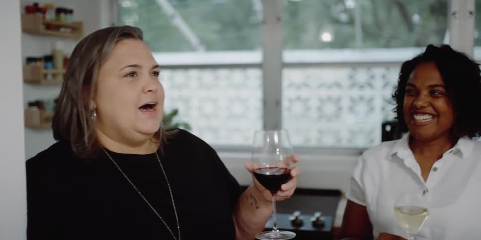 A group of friends talks to each other and drinks wine in the kitchen