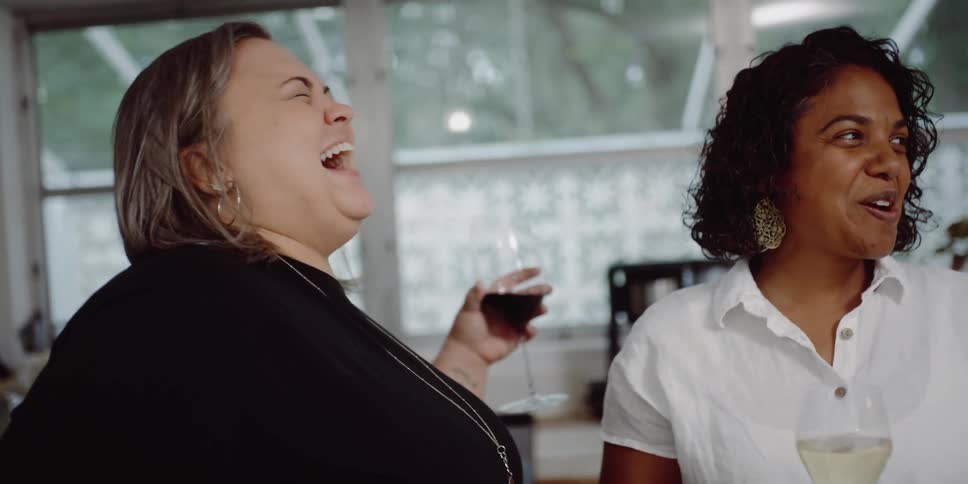 Two women holding wine glasses laugh and talk