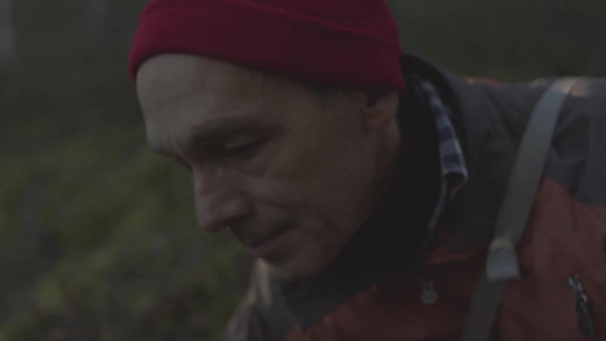 Close up of the face of a man wearing a red cap and jacket in the forest at morning