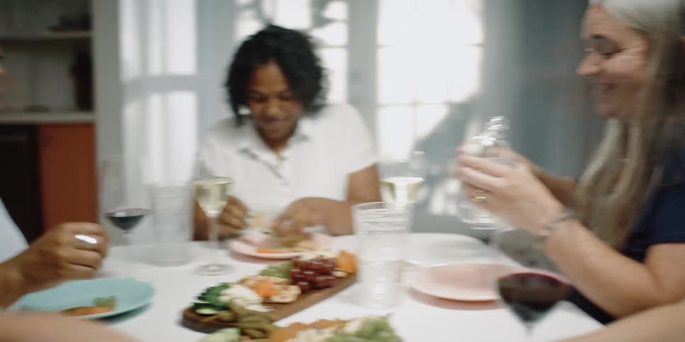 Female friends sit around dining table talking while eating cheese and drinking wine