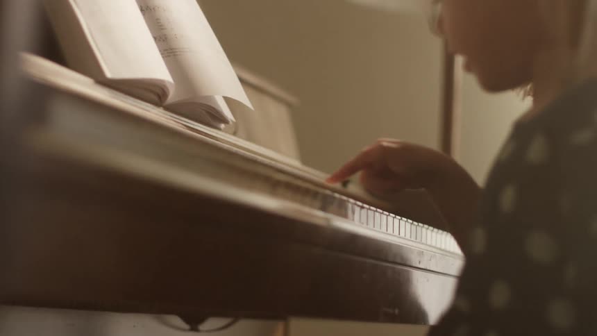 A little girl sits at a piano in front of sheet music and hits the keys with one finger