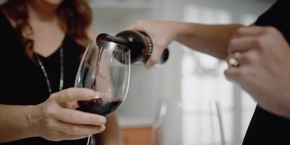 A mn pours wine from a bottle in a wine glass being held by a woman