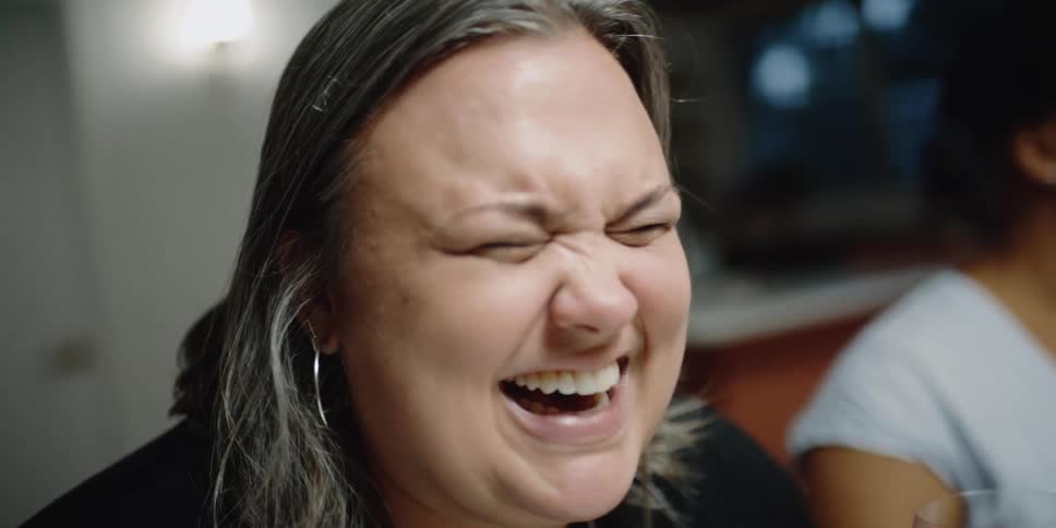A woman sits next to another woman in a home and laughs