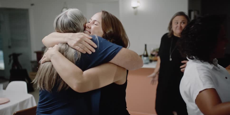 Several women are in a kitchen greeting and hugging each other
