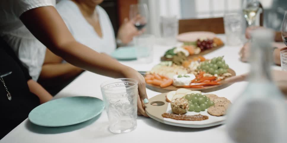 Black woman places a tray of appetizers on a table where other women are sitting and drinking wine