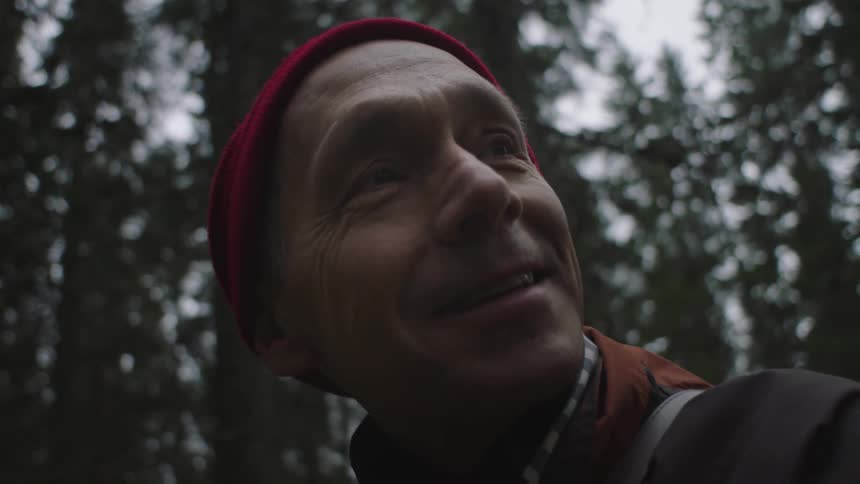 An elderly man in a forest smiles as he looks around