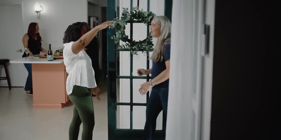 A woman opens her front door and hugs a friend as she walks inside