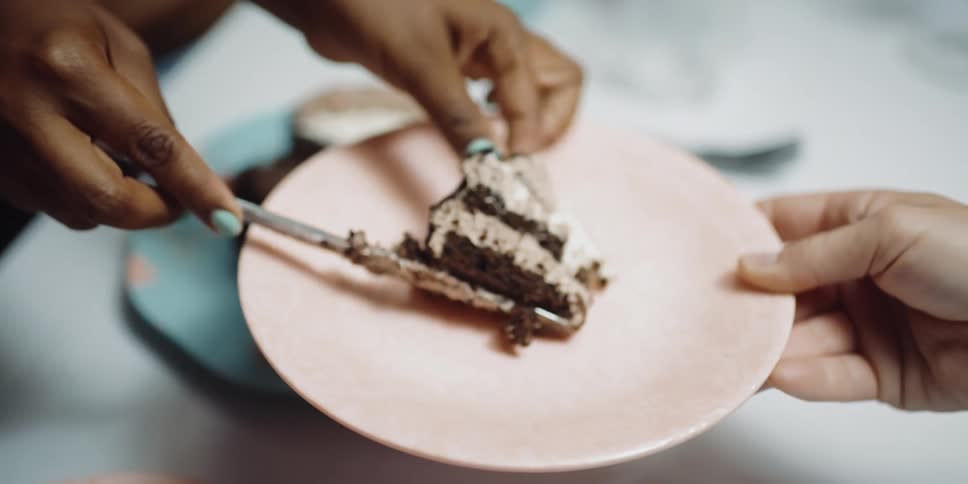 A woman uses a knife to place a slice of cake on a plate being held by another person