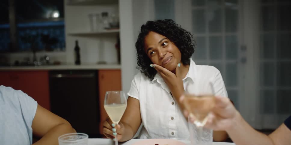 A group of women sit at a table in a kitchen drinking wine