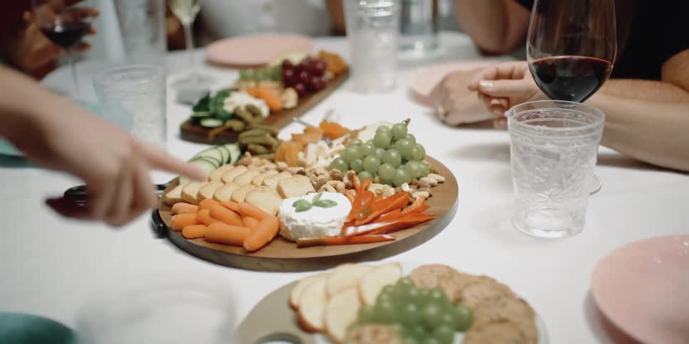 A hand points over to a plate of appetizers on a dining room table where people are sitting and eating