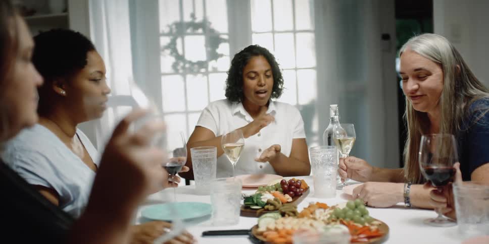 A group of friends sitting at table talks with each other drinking wine and eating