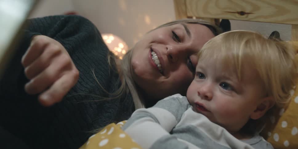 A woman reading a book to a boy in a bedroom