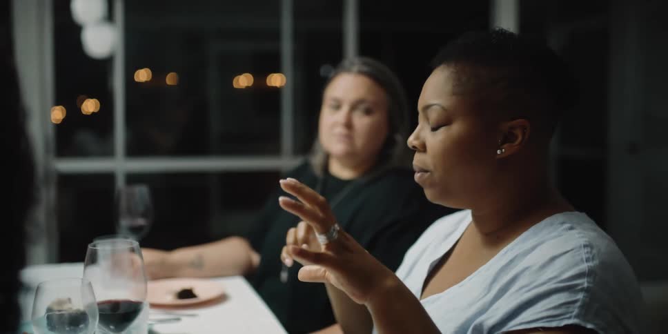 A woman talking with her hands sitting at a dinner table with guest at night time
