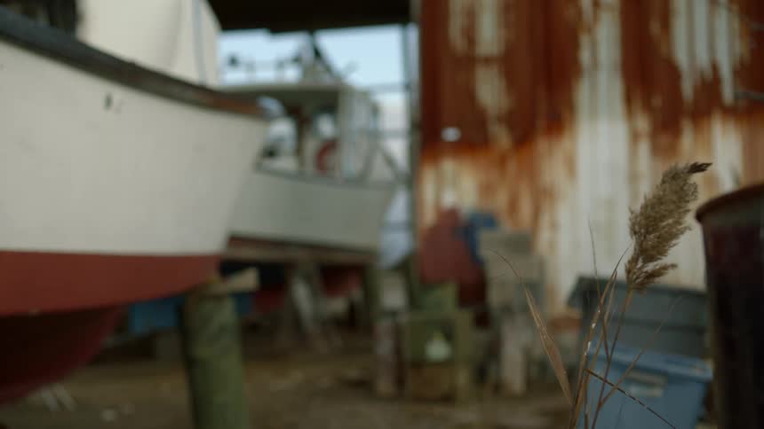 Private boats are dry docked in a rusty garage on a breezy evening
