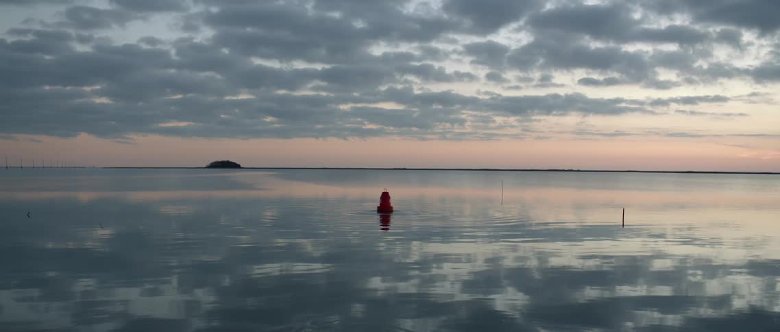 A red buoy floating on flat water at sunset is mysteriously moved by something underwater
