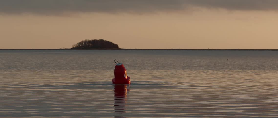 A mysterious red buoy moves by itself on flat water. at sunset
