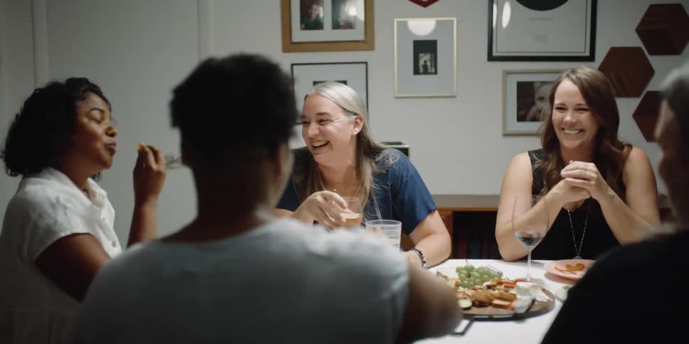 A group of female friends laugh over drinks and appetizers at a dinner party at home