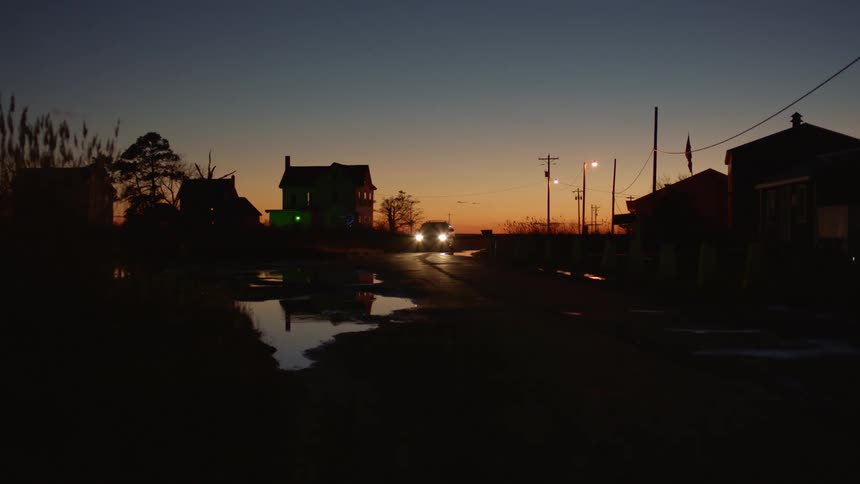 A car drives through a flooded neighborhood at sunset