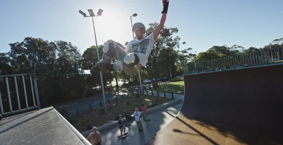Young man jumping on a half pipe skateboard ramp in the park at morning