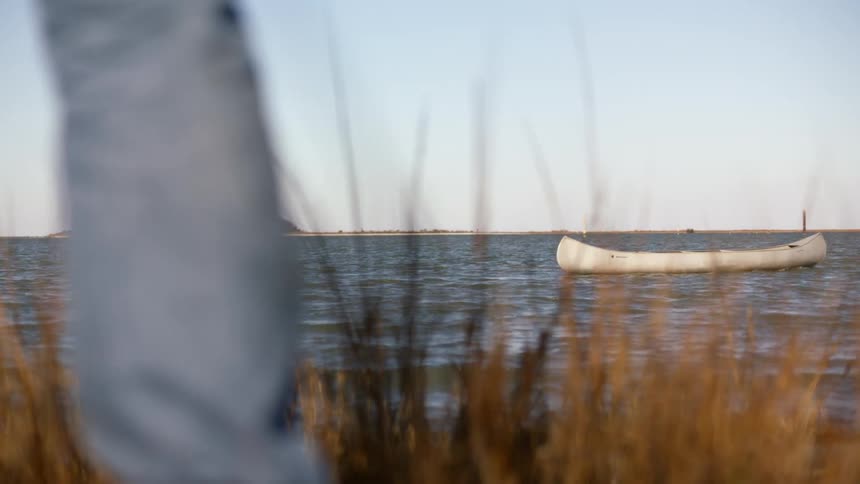An empty row boat moves across the water by itself while someone watches