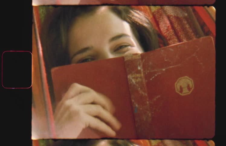 A woman is sitting with a book hiding behind it and smiling