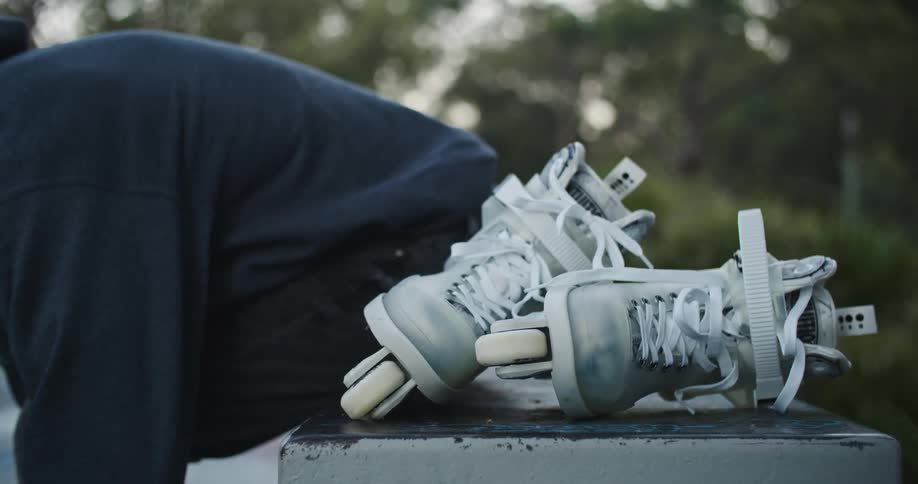 A person ties their shoes on a park bench after taking their roller blades off