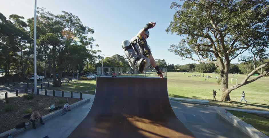 A person with inline skates skating in a skate park with trees the sky and clouds in the background