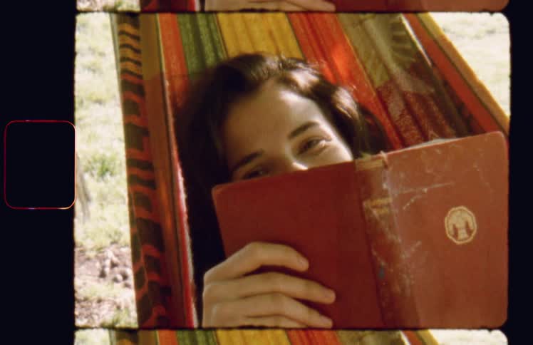 Woman lying in hammock covers face partially with book and smiles