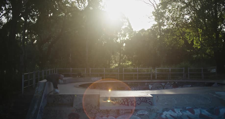 Man sitting in a skate park near the trees at sunset